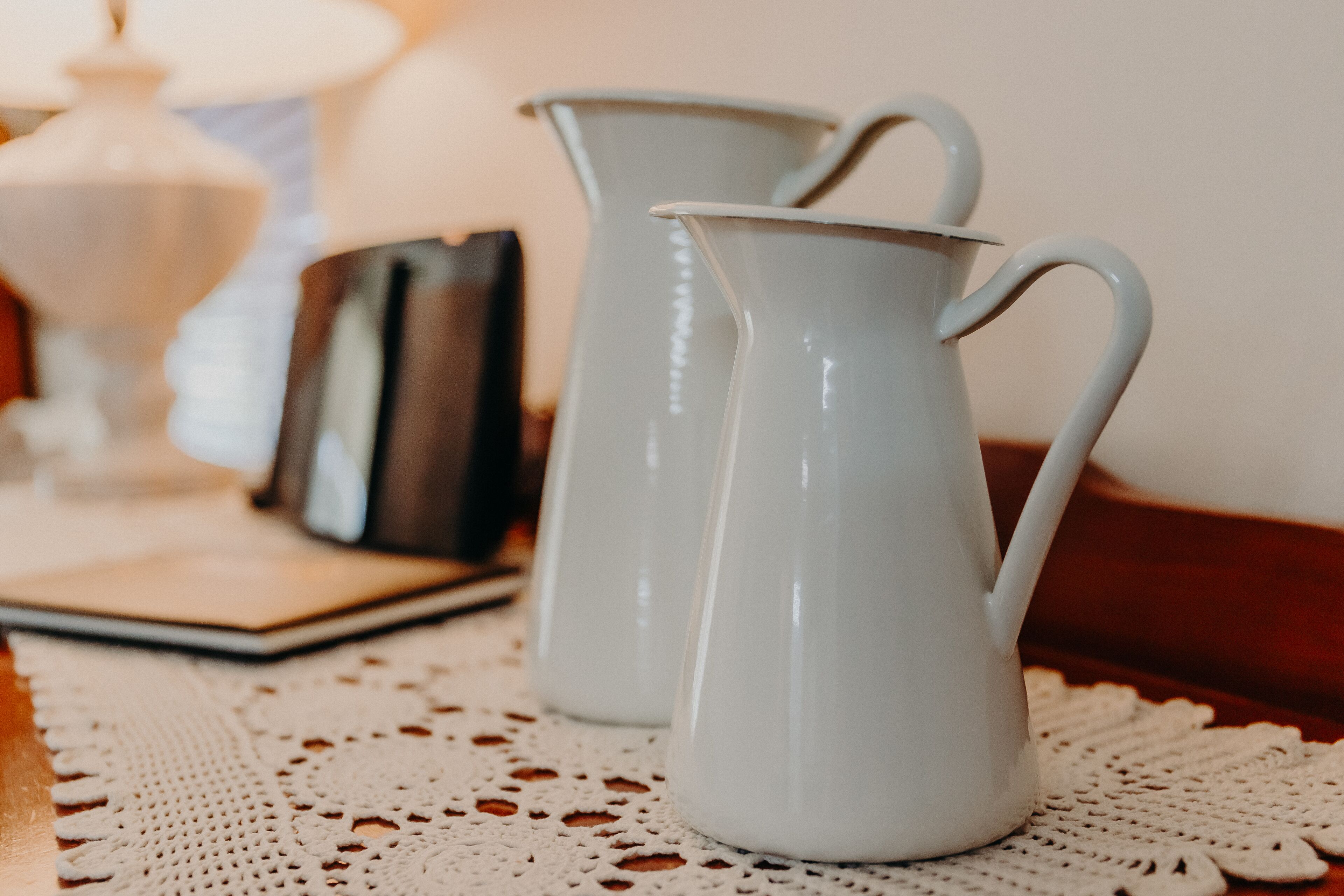 Two white ceramic pitchers on a white doily.