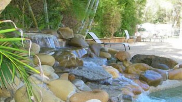 A natural water feature with rocks and a small waterfall, surrounded by greenery and outdoor furniture. - Lighthouse Beach Holiday Village (Port Macquarie)