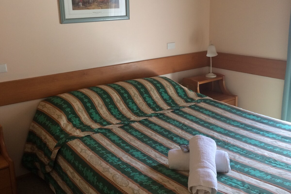 A hotel room with a bed, a nightstand, a lamp, and a framed picture on the wall.