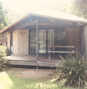 A wooden cabin with a covered porch and a bench. - Lighthouse Beach Holiday Village (Port Macquarie)