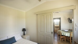 Un dormitorio con cama, mesita de noche, lámpara y puerta que da a un comedor con mesa y sillas.