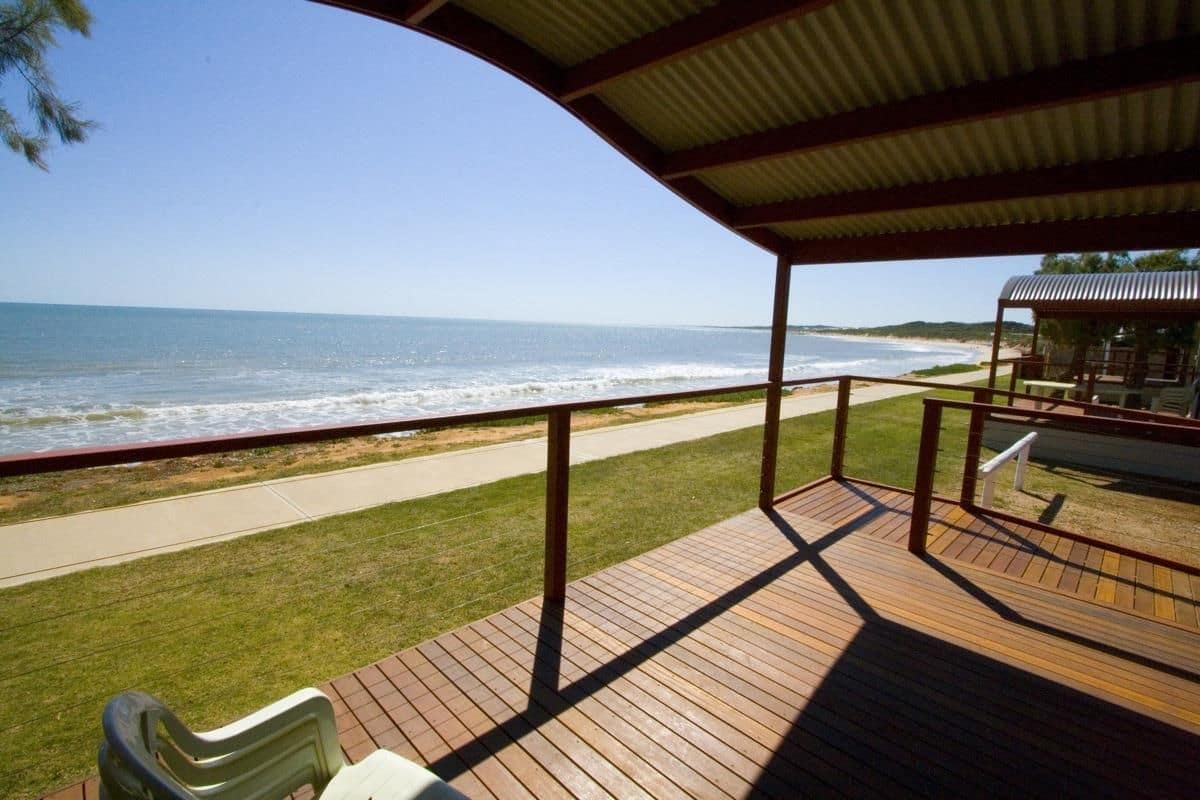Eine Holzterrasse mit Blick auf das Meer, ein Weg und ein überdachter Bereich mit Stühlen.