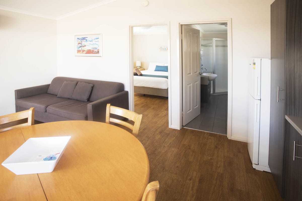 Ein kompakter Wohnbereich mit Sofa, Esstisch und Küchenzeile inklusive Kühlschrank und Spüle.