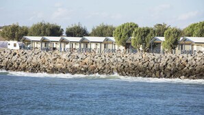 Una hilera de cabañas frente a la playa, con una costa rocosa y olas rompiendo al fondo.