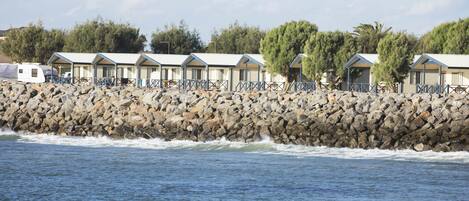 A row of beachside cottages with a rocky shoreline and waves crashing in the background.