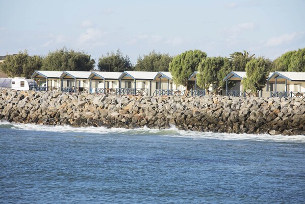 A row of beachside cottages with a rocky shoreline and waves crashing in the background.