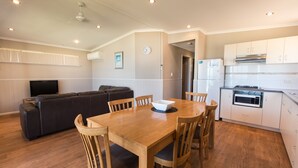Un espacio habitable compacto con zona de comedor, sofá, televisor y cocina con armarios y electrodomésticos blancos.