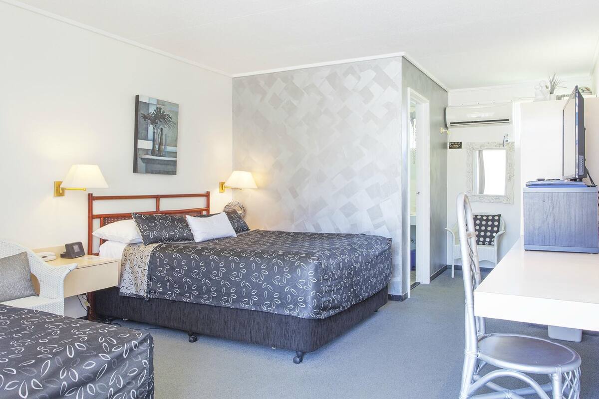 Una habitación de hotel con una cama, mesitas de noche, un escritorio y una silla.