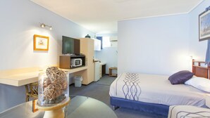 Una habitación de hotel con cama, escritorio con computadora, microondas y pequeña kitchenette.