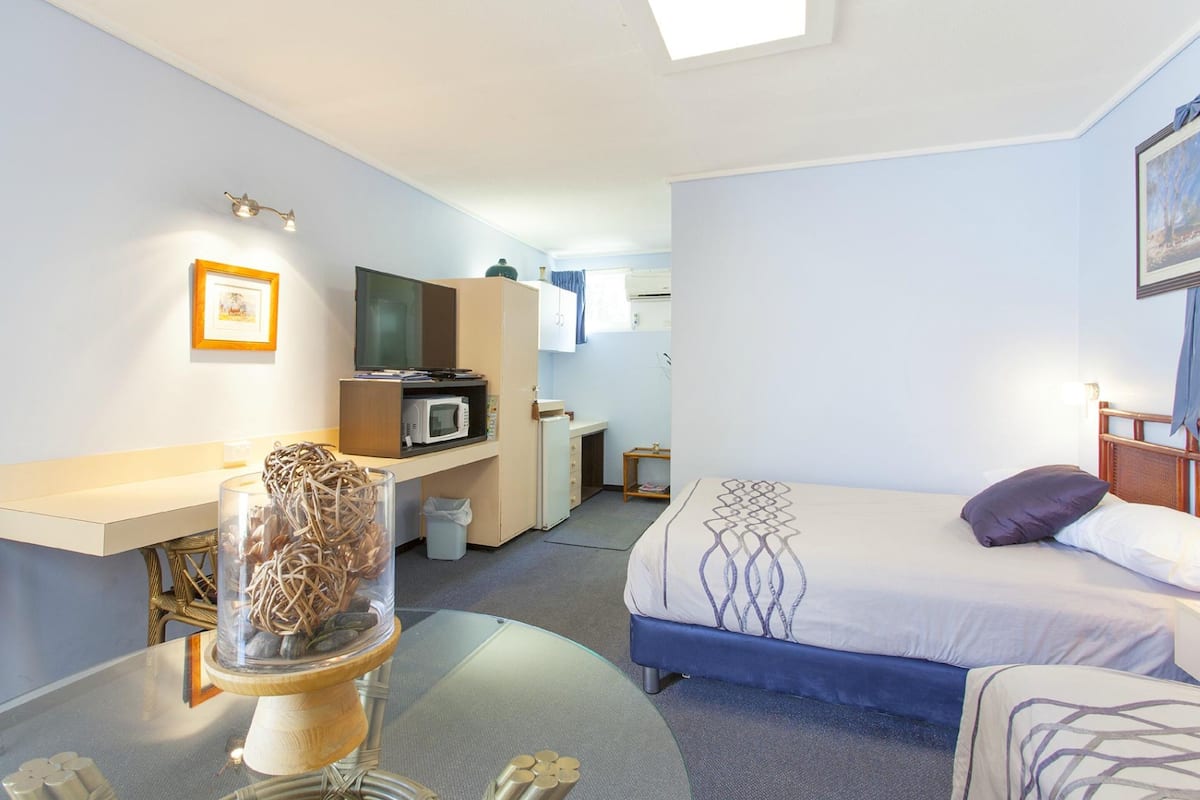 Una habitación de hotel con cama, escritorio con computadora, microondas y pequeña kitchenette.