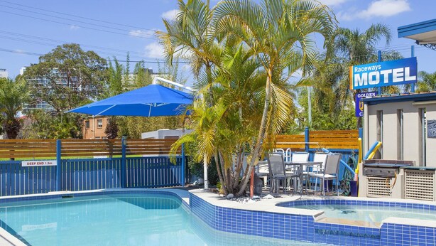 Una piscina con borde de azulejos azules, una sombrilla azul y un cartel del Motel Raceways.