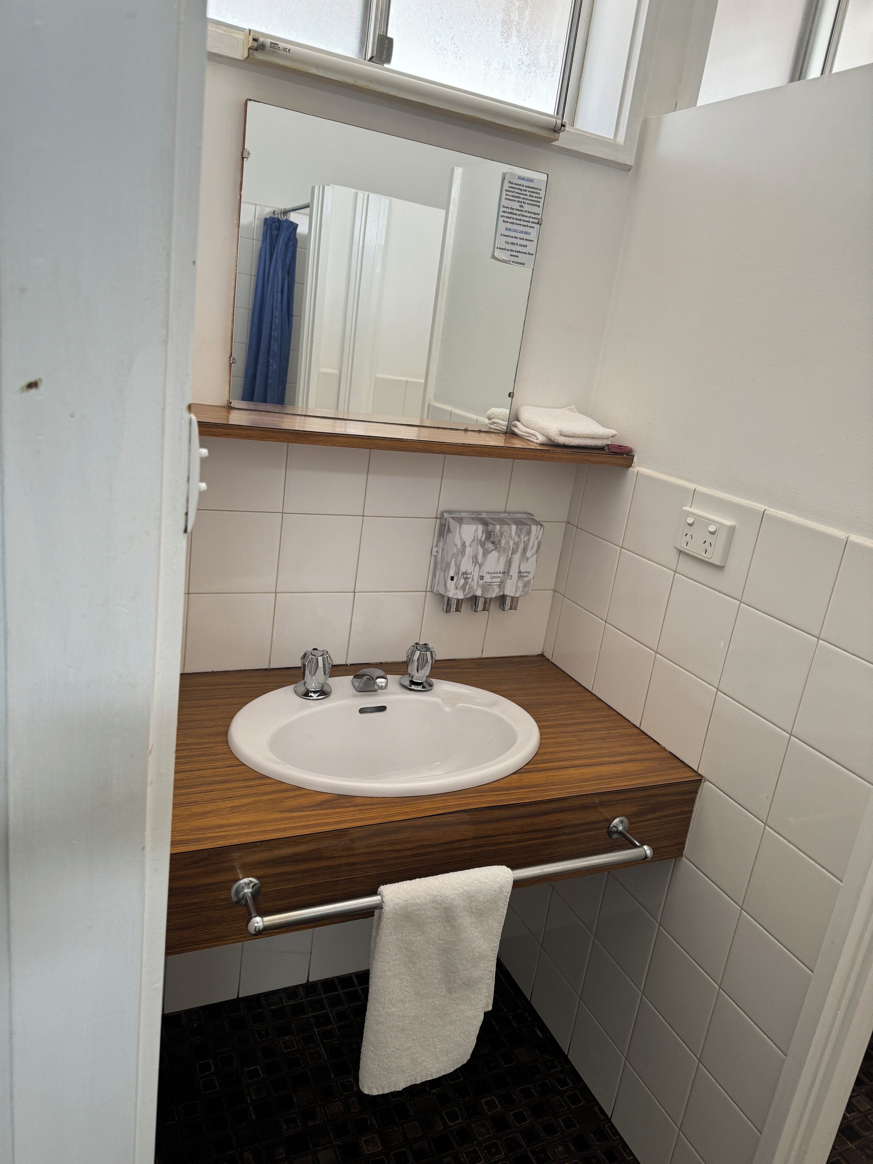 Un baño con tocador de madera, un lavabo blanco, un espejo y un perchero para toallas.