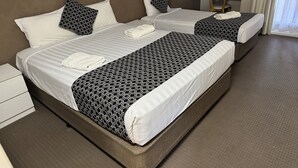 A hotel room with two beds, each with a patterned bedspread and white pillows. There is a small desk with a chair and a window with curtains. - Mid City Plantation Motel (Mildura)
