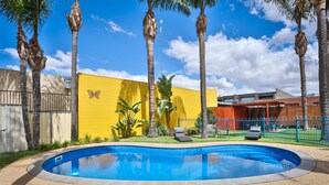 A swimming pool surrounded by palm trees and a yellow wall with a butterfly design. - Mid City Plantation Motel (Mildura)