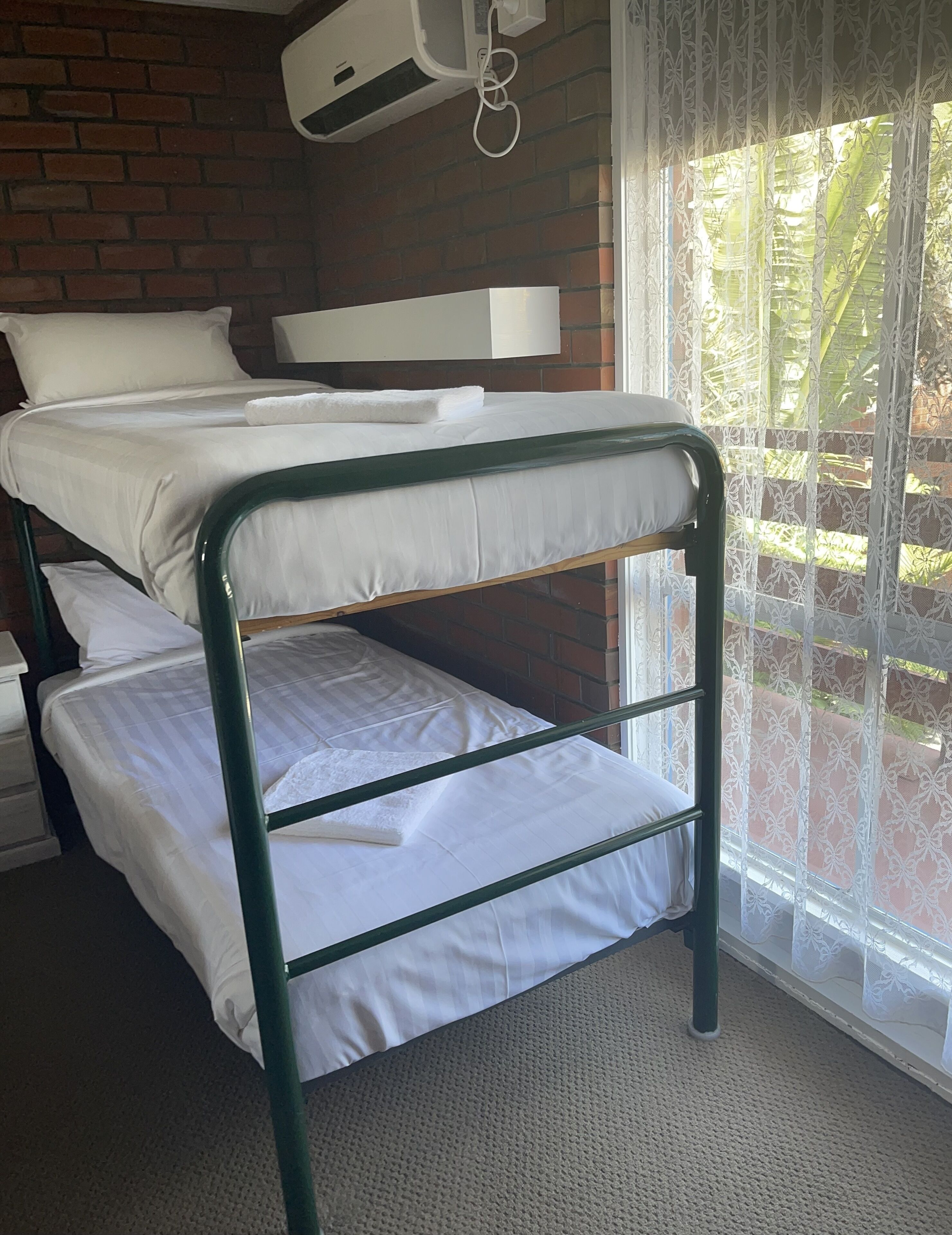 A bunk bed with white bedding in a room with a brick wall and a window with lace curtains.
