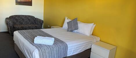 A hotel room with a bed, a nightstand, a lamp, a leopard print sofa, and a painting on the wall.