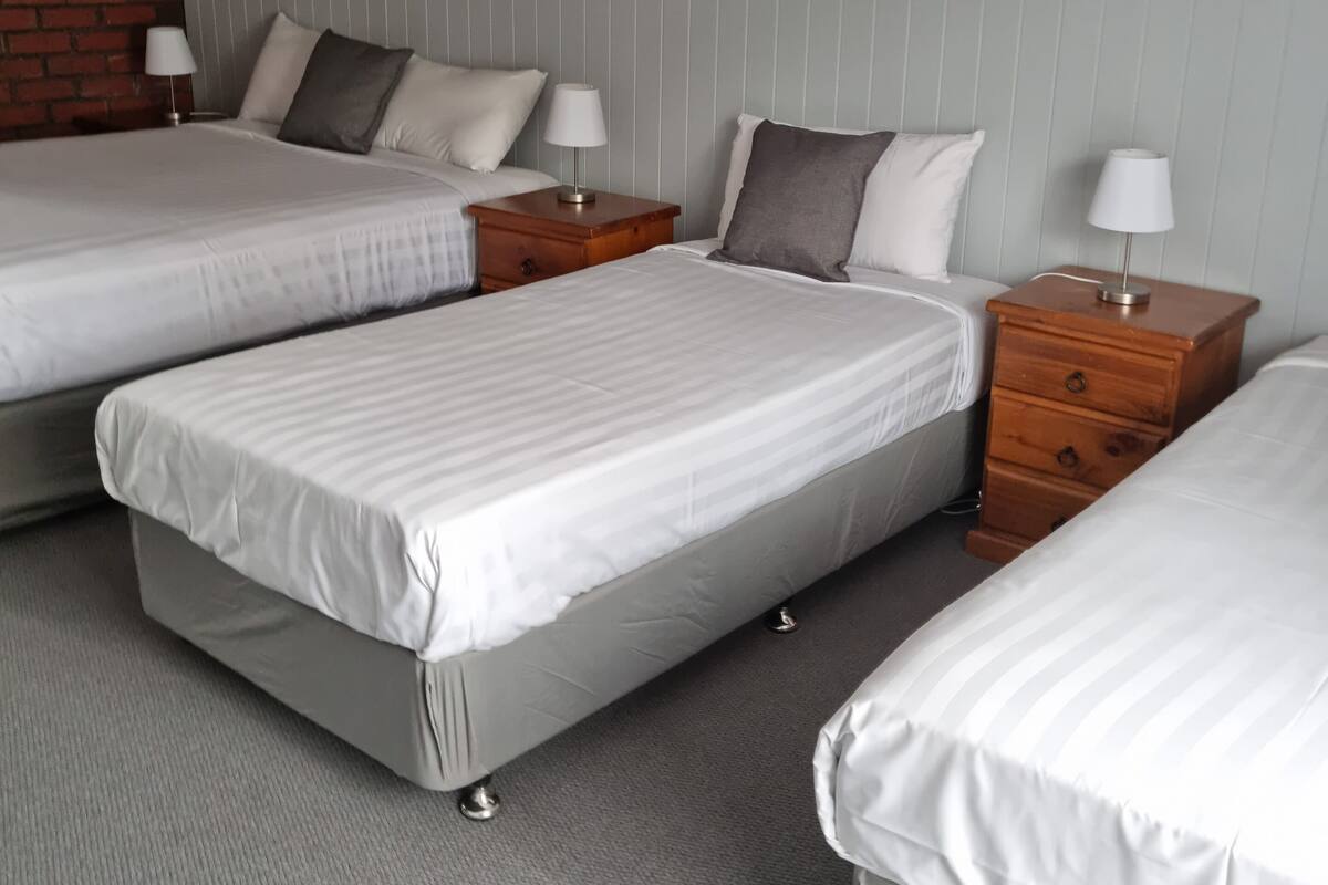 A hotel room with three beds, wooden nightstands, and a brick wall.