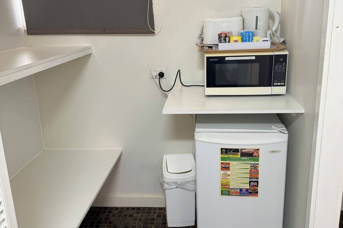 A compact kitchenette with a microwave, a small refrigerator, and a trash bin.