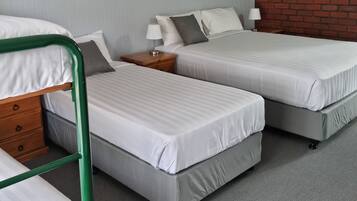 Una habitación con dos camas individuales, una cama litera de metal verde y una pared de ladrillo, además de un techo blanco.