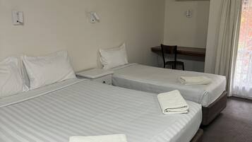 A hotel room with two beds, a desk, and an air conditioning unit.