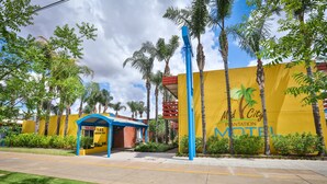 A hotel entrance with a yellow wall, palm trees, and a blue canopy. - Mid City Plantation Motel (Mildura)