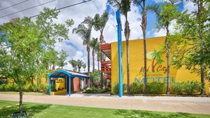 A motel with a yellow exterior and a blue awning, surrounded by palm trees and greenery. - Mid City Plantation Motel (Mildura)