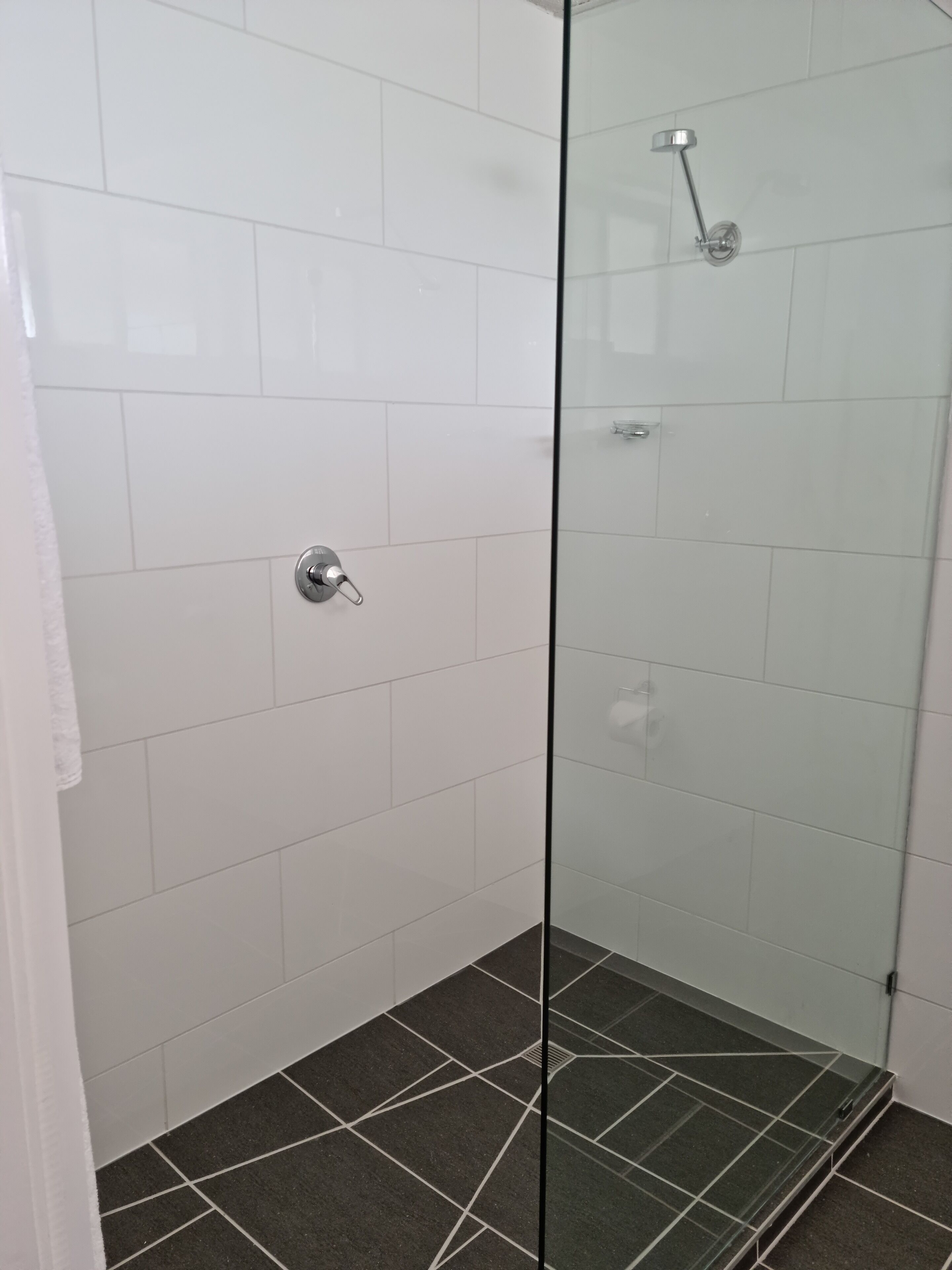 Ducha con paredes de cristal, azulejos blancos y suelo oscuro.