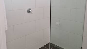 Ducha con paredes de cristal, azulejos blancos y suelo oscuro.