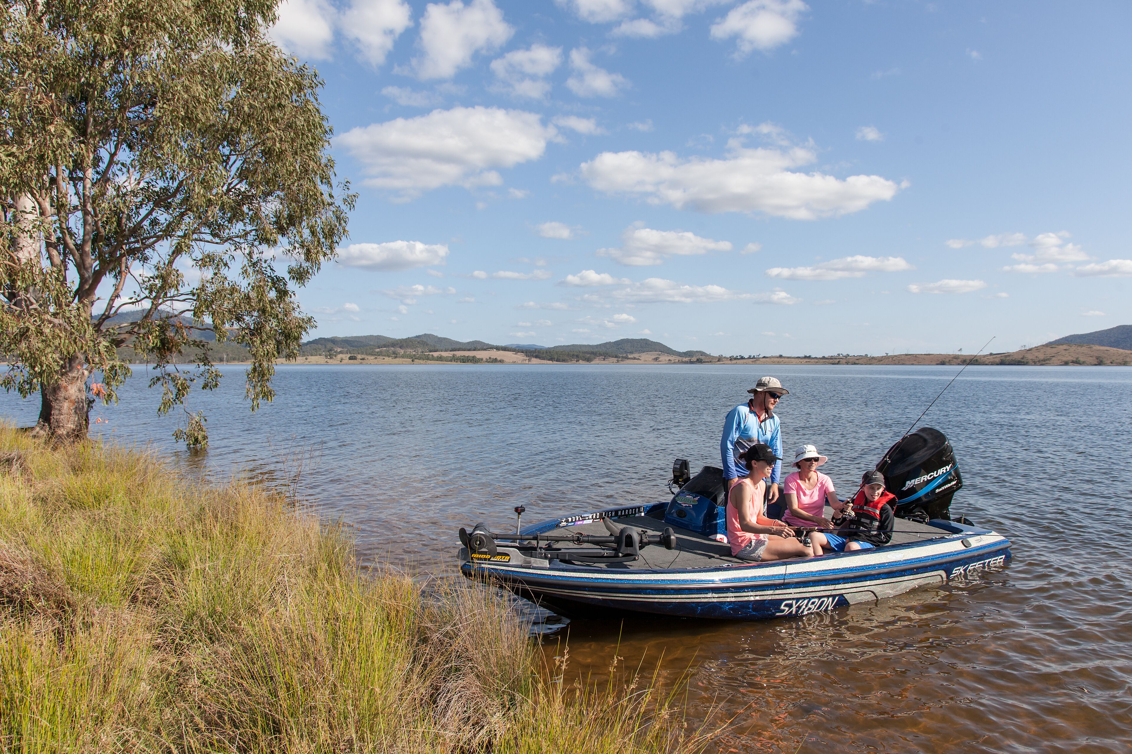 Un petit bateau à moteur avec quatre personnes à bord, naviguant sur un lac paisible, entouré de collines.