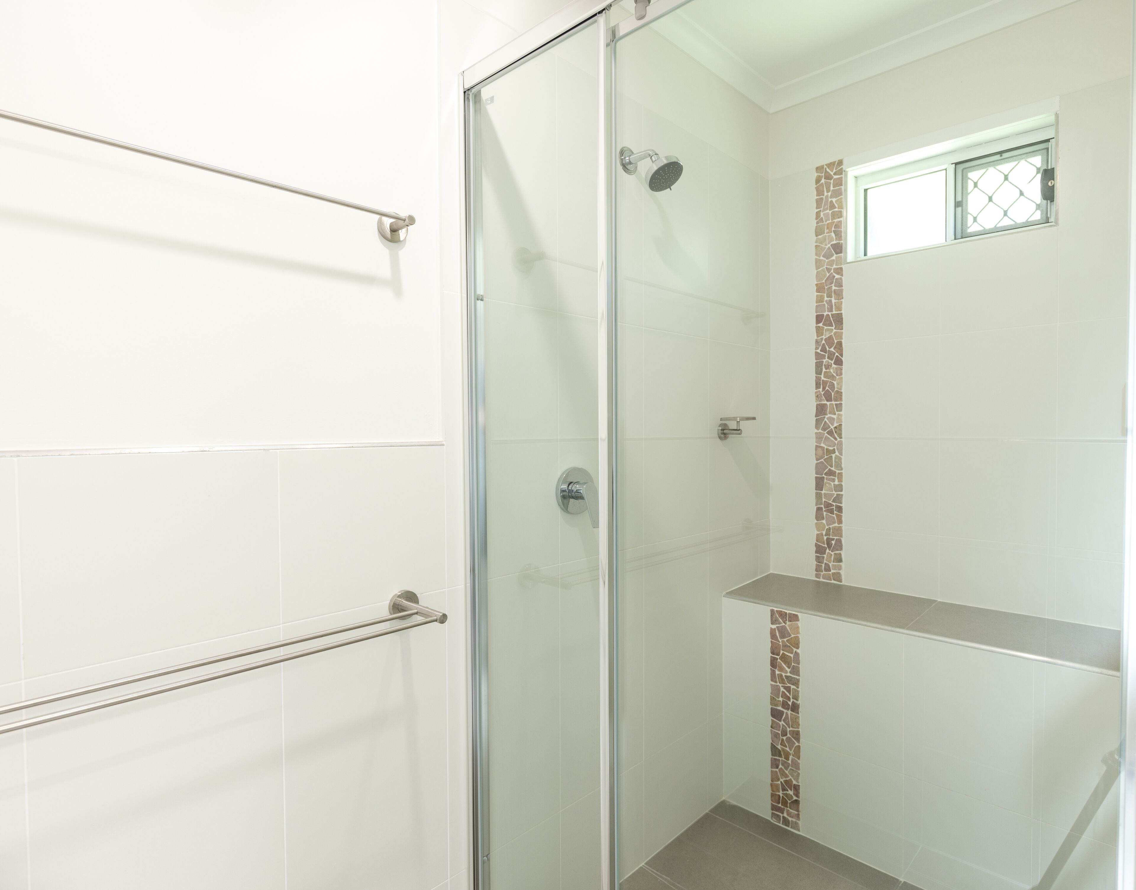 Ducha con mampara de vidrio, cabezal de ducha de mano, toallero y una ventana pequeña.