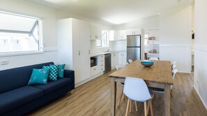A modern kitchen with white cabinets, a wooden dining table, and a blue sofa with teal cushions. - NRMA Lake Somerset Holiday Park (Hazeldean)