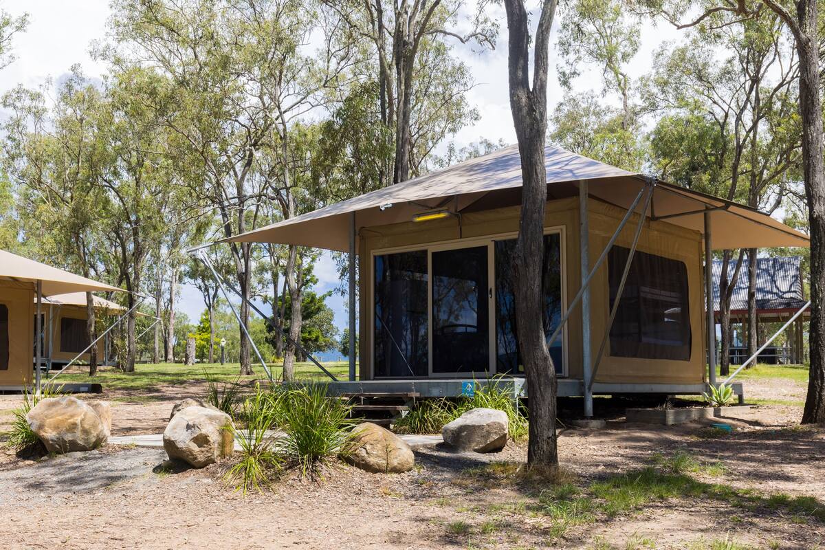A camping site with a large tent and a smaller structure, surrounded by trees and rocks.