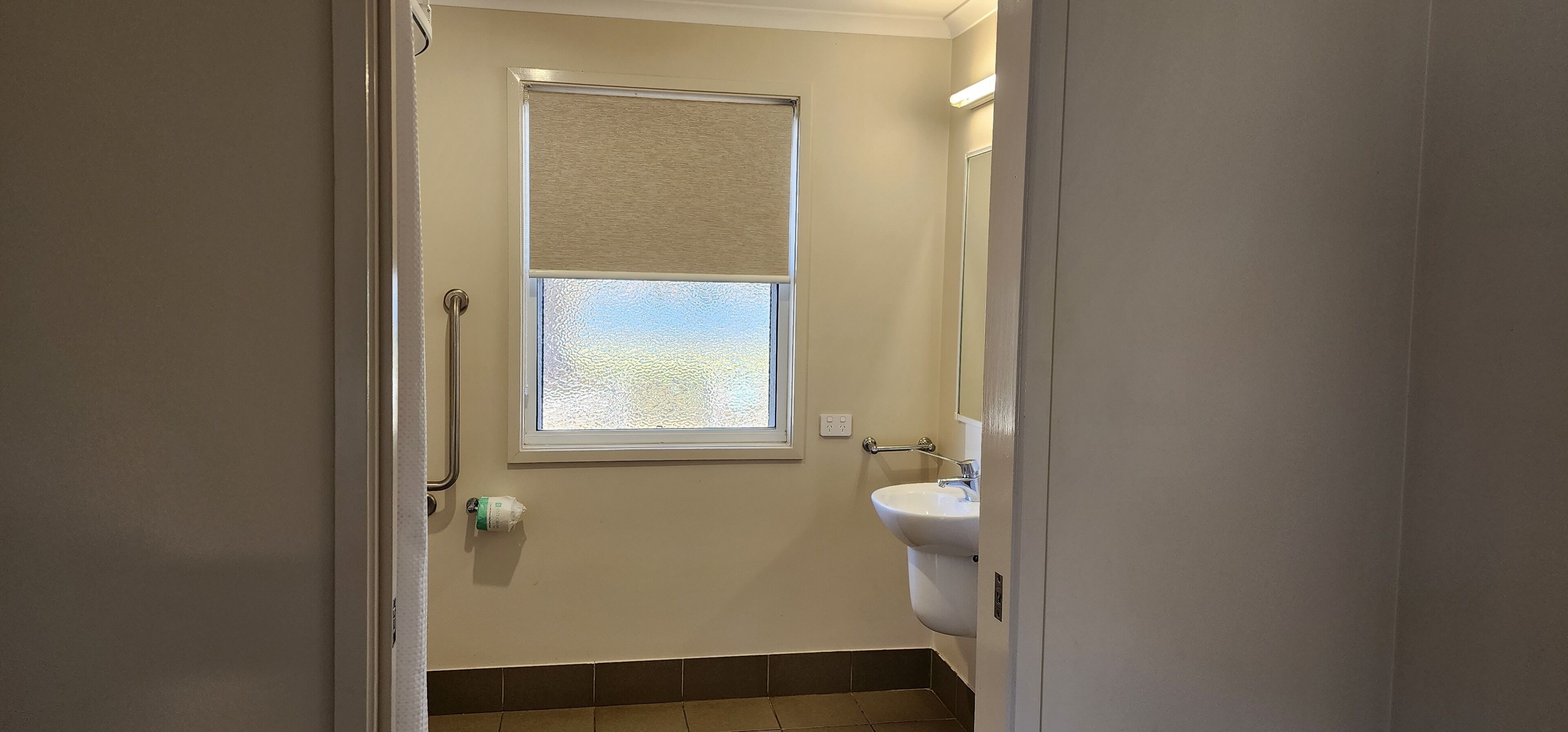 Un baño con ventana, lavamanos y un perchero para toallas.