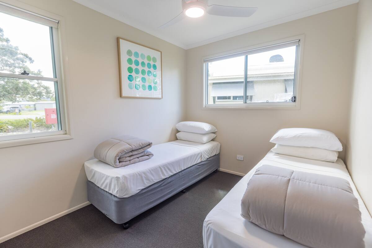A small, clean room with two single beds, a large window, and a ceiling fan.