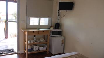 Una kitchenette pequeña con microondas, cafetera y estantes con vajilla.