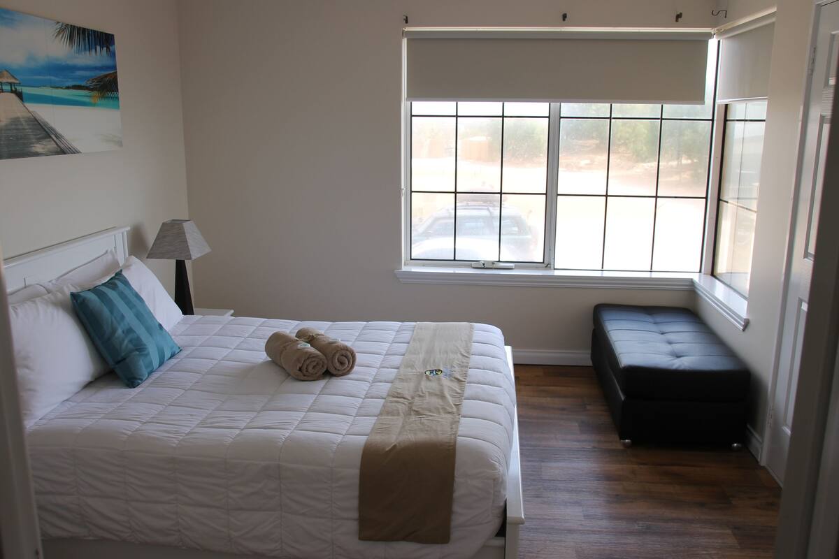 A bedroom with a bed, a bench, a window, and a painting on the wall.