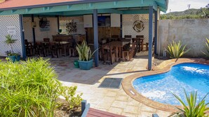 Un espacio al aire libre techado con piscina, muebles de madera y plantas en macetas.
