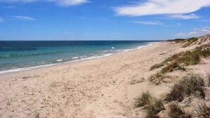 Una playa arenosa con olas suaves y vegetación escasa.