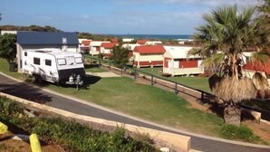 Una caravana estacionada en un área verde con vistas a la costa y varios edificios con tejados rojos.