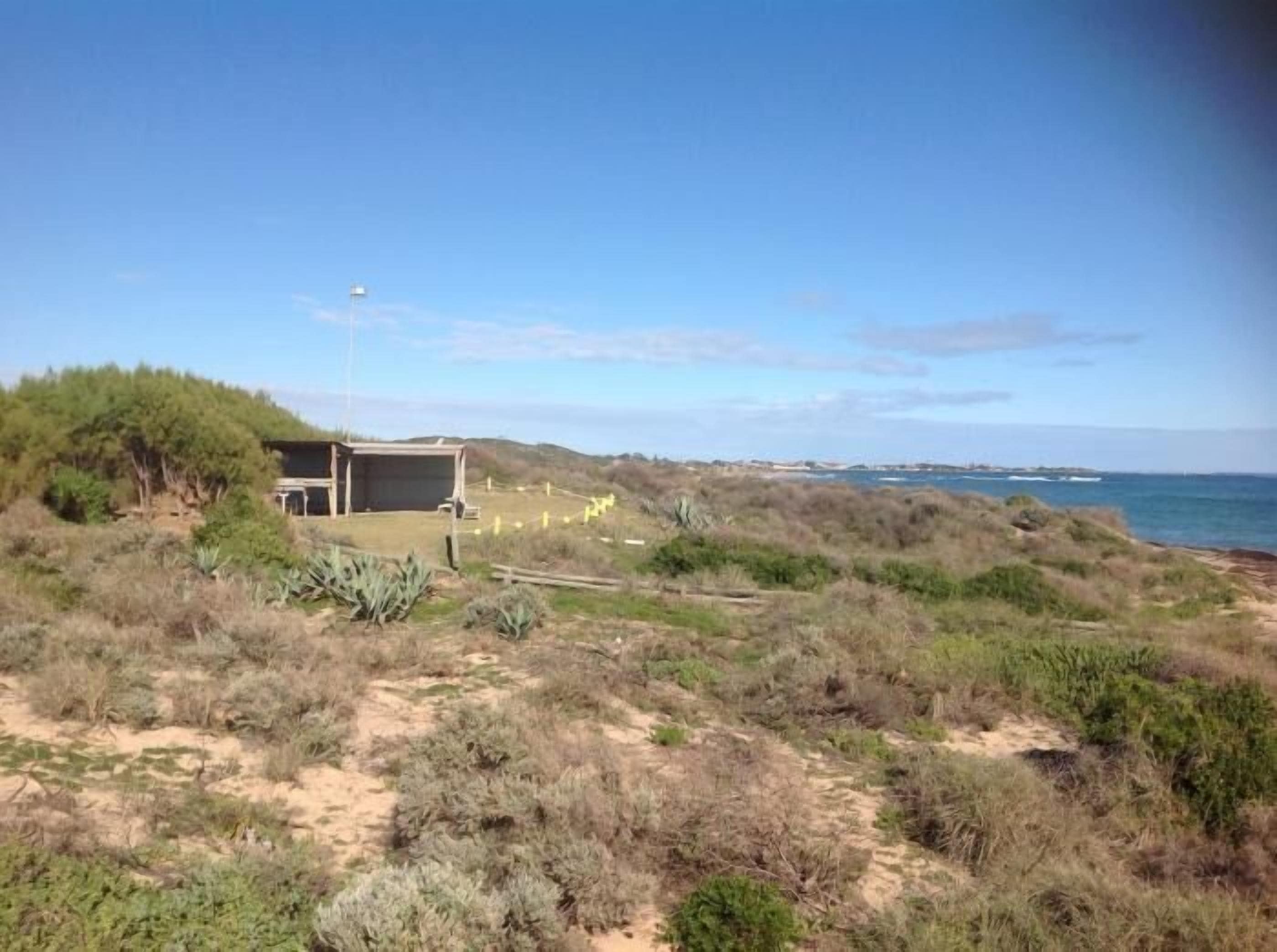 A coastal landscape with a building, possibly a hotel, surrounded by natural vegetation and a view of the sea.