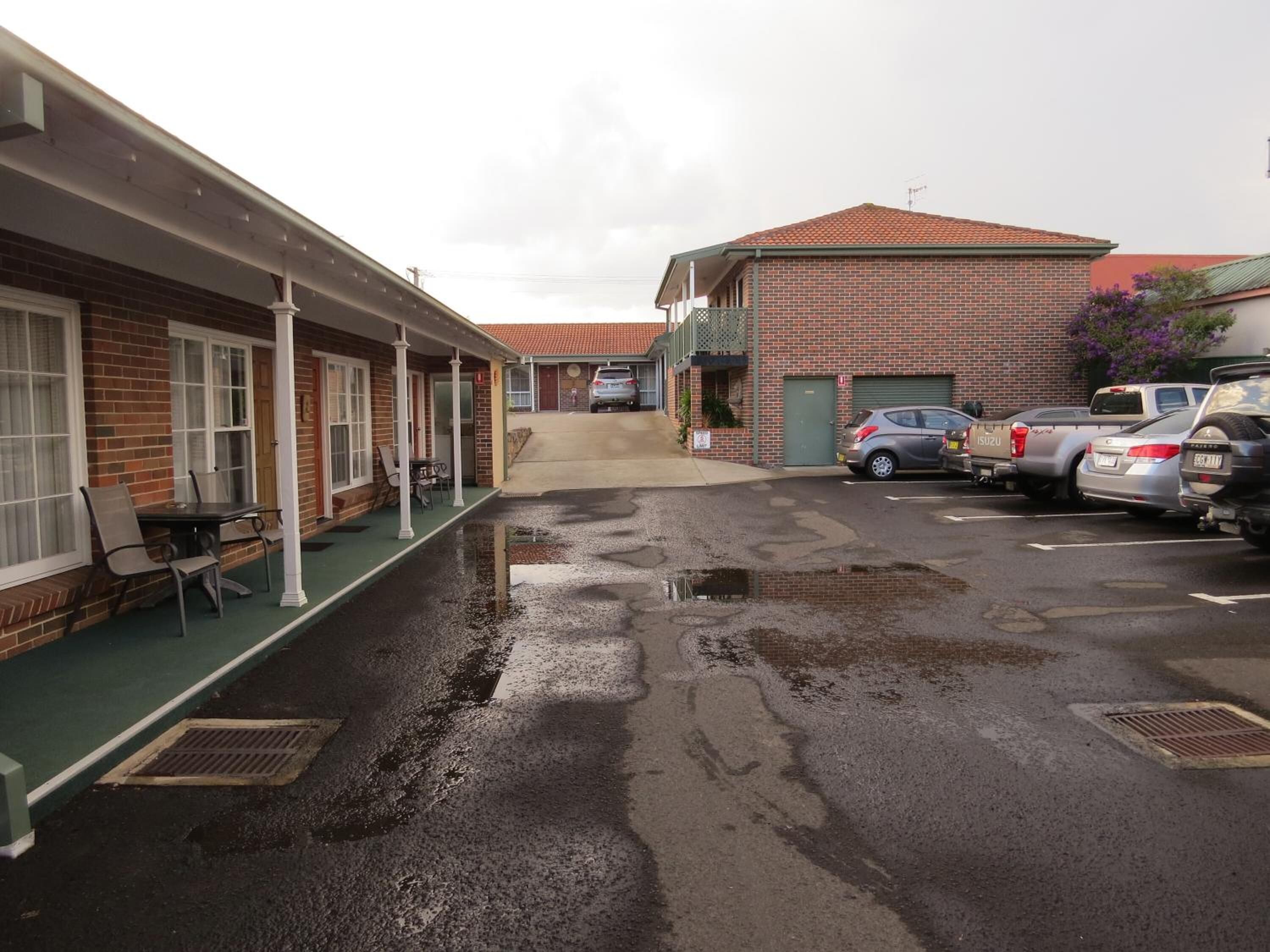 Un motel con zona de estar al aire libre cubierta, edificio de ladrillo y aparcamiento con varios coches.