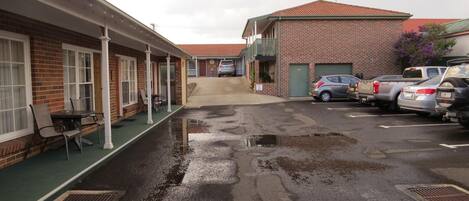 Un motel con zona de estar al aire libre cubierta, edificio de ladrillo y aparcamiento con varios coches.