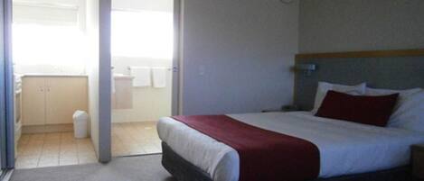A hotel room with a bed, a bathroom, and a view of the outside.