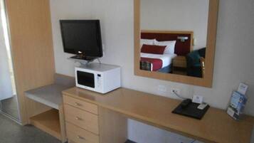 Habitación de hotel con escritorio de madera, televisión de pantalla plana, microondas, espejo y cama con ropa de cama roja y blanca.