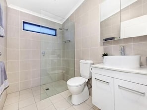 A modern bathroom with a glass-enclosed shower, a toilet, and a vanity with a sink and mirror.