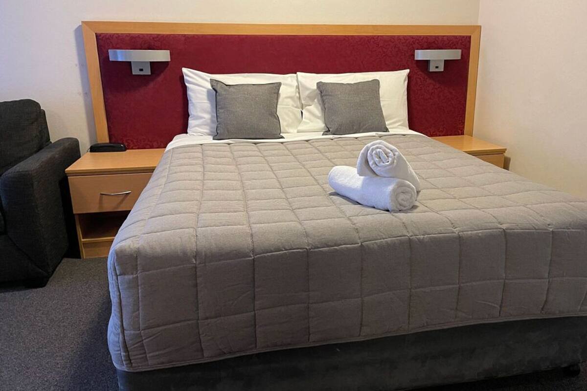 Une chambre d’hôtel avec un grand lit, une table de chevet en bois, un bureau et une chaise.