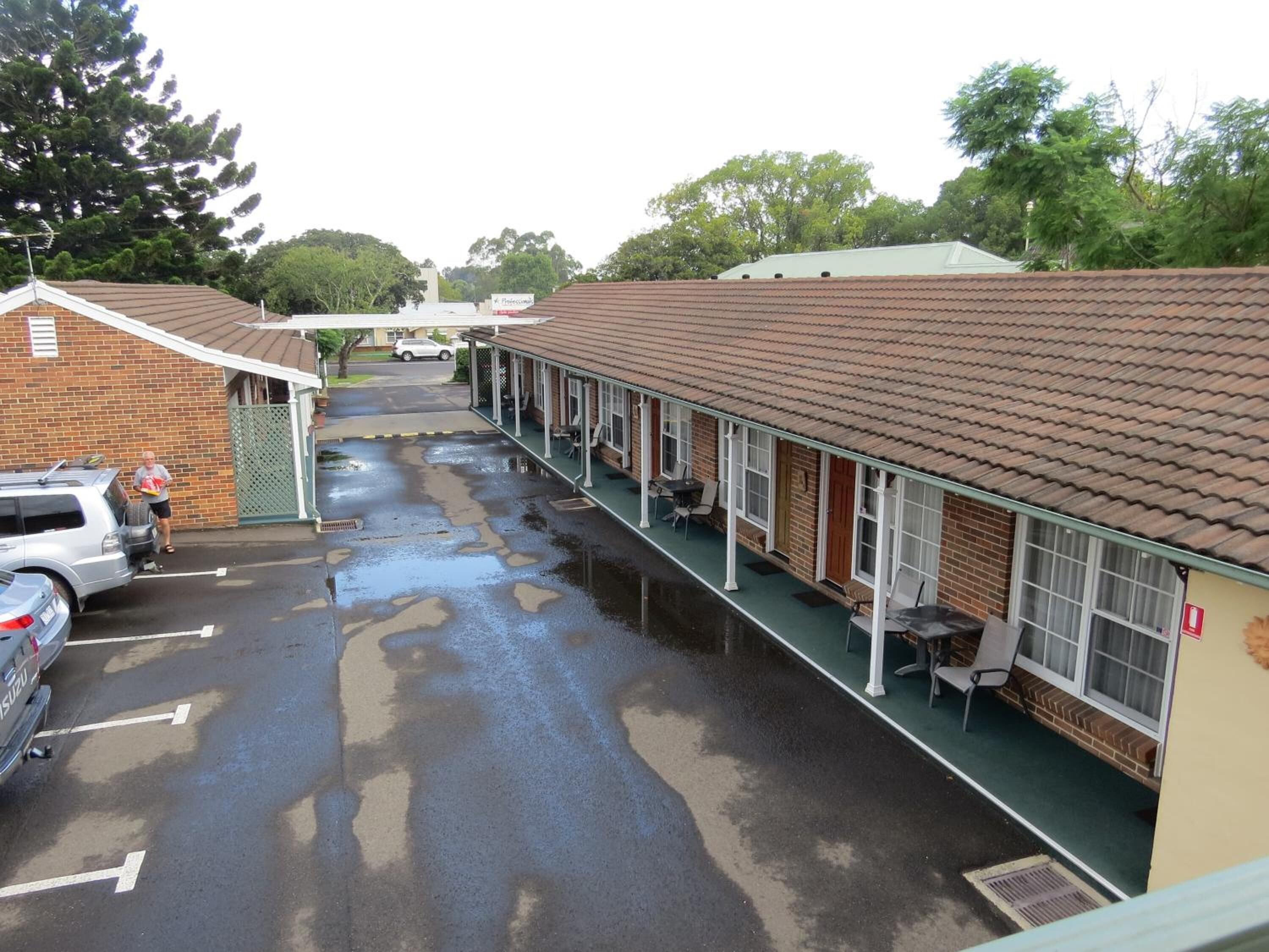 A motel with a covered outdoor seating area, a brick building, and a parking lot with a car.