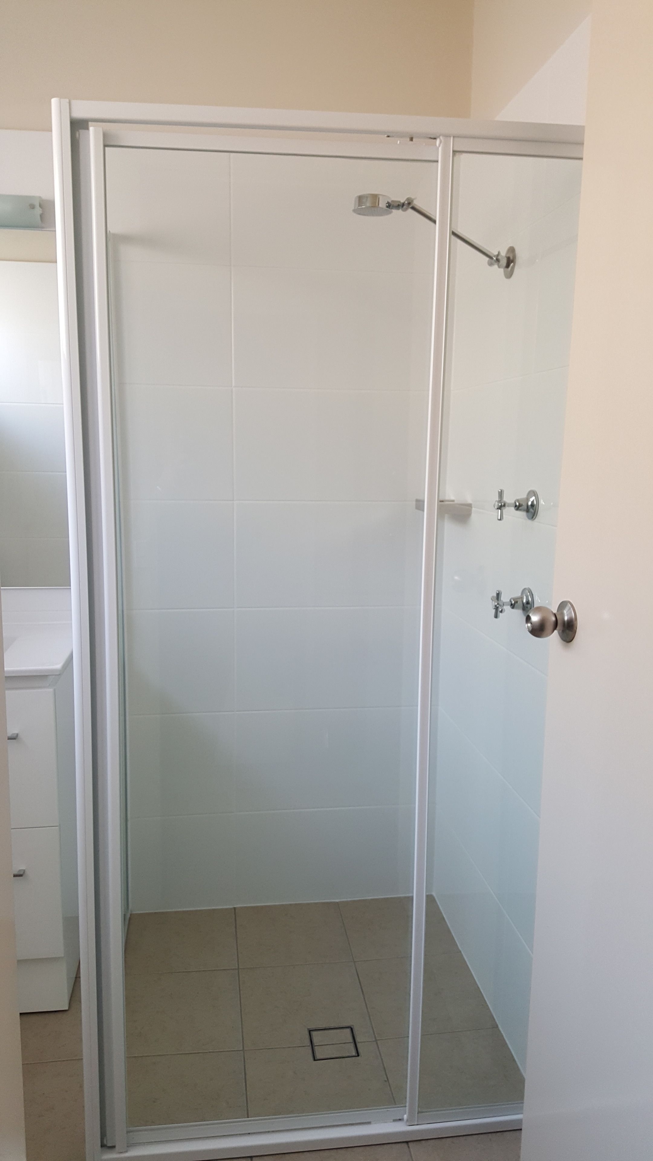 A glass-enclosed shower stall with a white tiled floor and a door with a round handle.