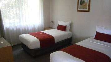 A hotel room with two beds, a nightstand, a lamp, and a window with sheer curtains.
