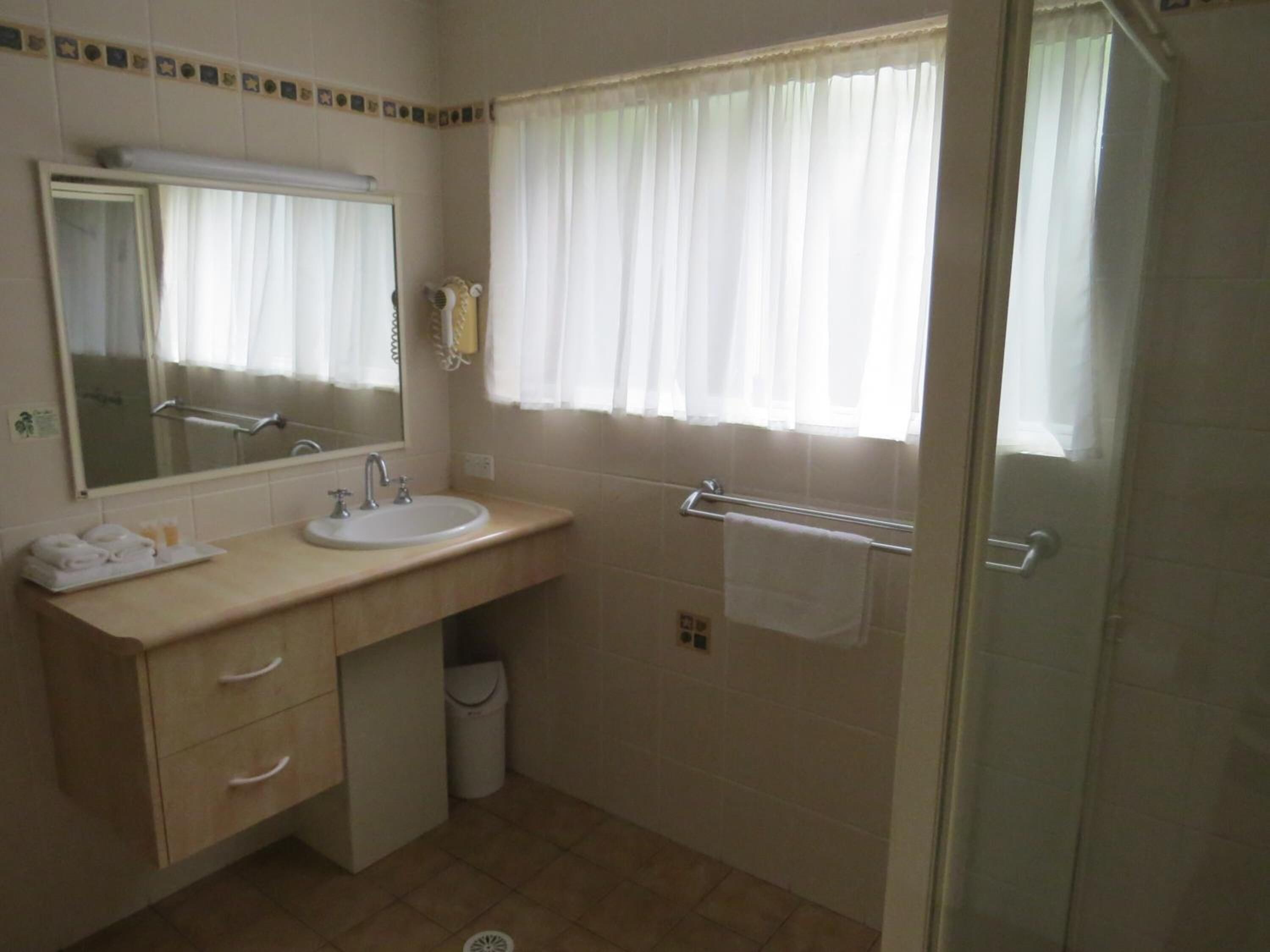 A bathroom with a sink, mirror, towel rack, and a shower area.